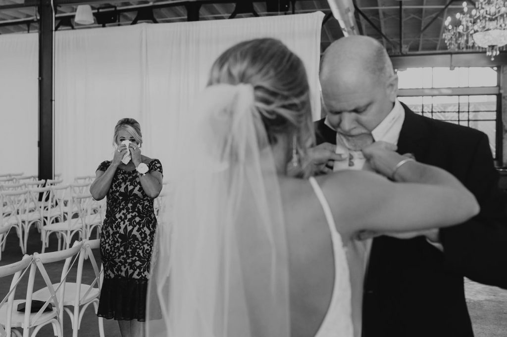 Documentary wedding photographer captured mother of bride crying as bride fixes her dad's tie.