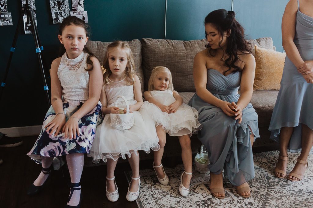 Documentary wedding photographer. Three young girls sitting on a sofa, looking bored, waiting for the wedding ceremony to begin