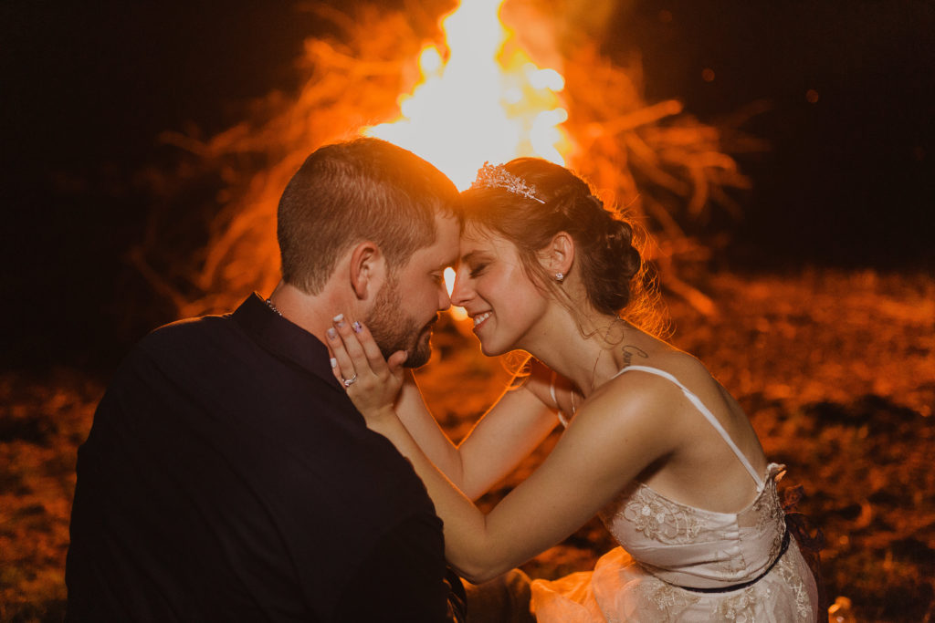 couple keeping warm in front of the fire at a summer wedding